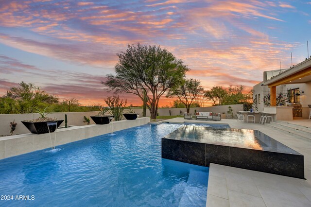 pool at dusk with a patio area, an outdoor kitchen, and pool water feature