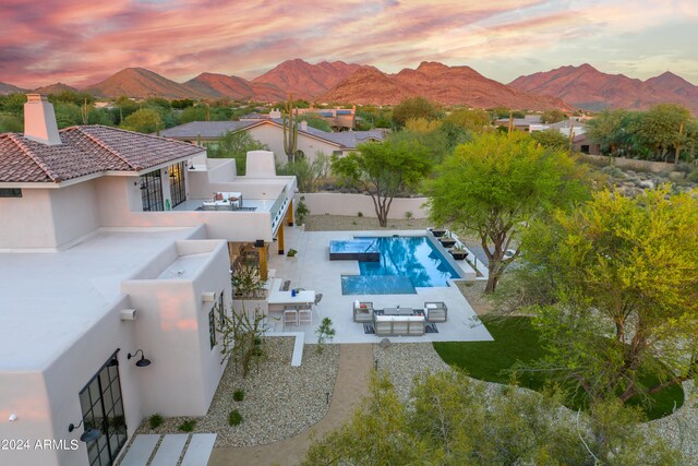 pool at dusk with a mountain view, an outdoor living space, a patio, a bar, and area for grilling