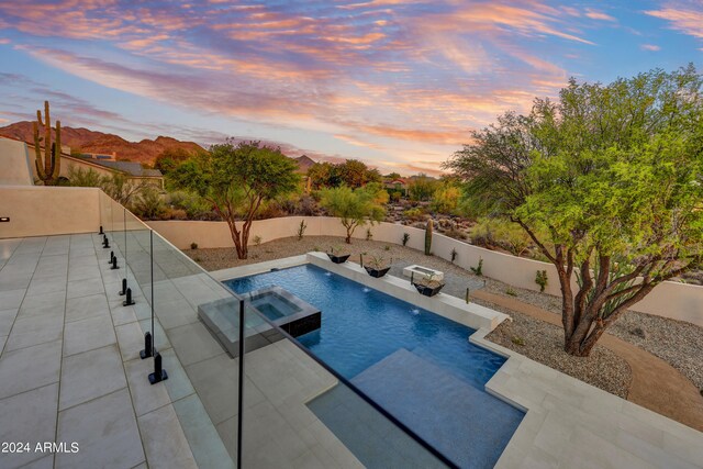 pool at dusk featuring an in ground hot tub and a patio