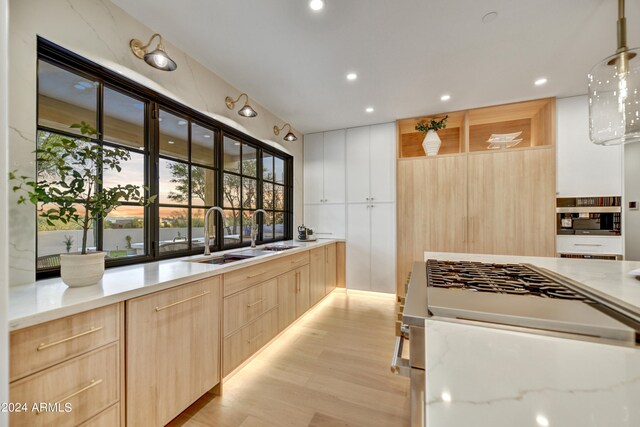 kitchen with light hardwood / wood-style flooring, light stone counters, decorative light fixtures, and sink