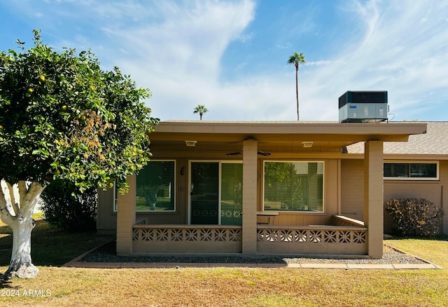 back of property with central air condition unit, a lawn, and covered porch