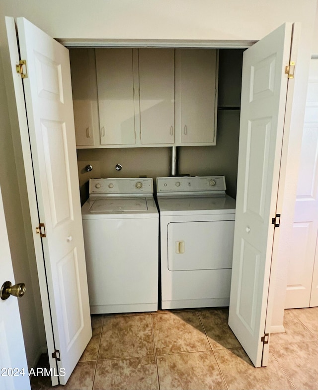 clothes washing area featuring washer and clothes dryer, light tile patterned floors, and cabinets