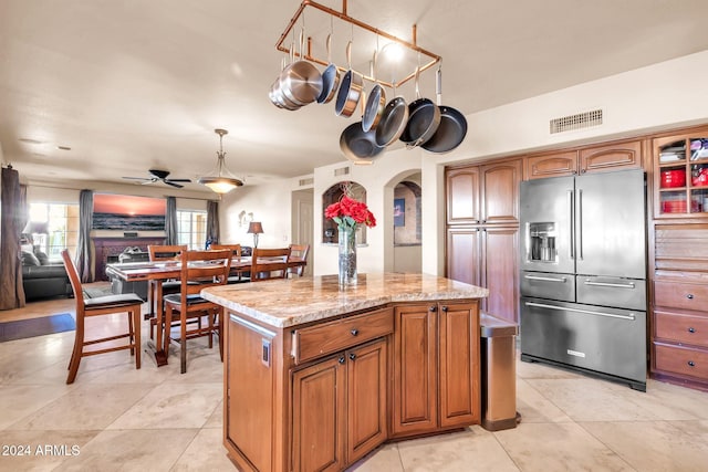 kitchen featuring a kitchen island, hanging light fixtures, light tile patterned floors, light stone countertops, and high end fridge