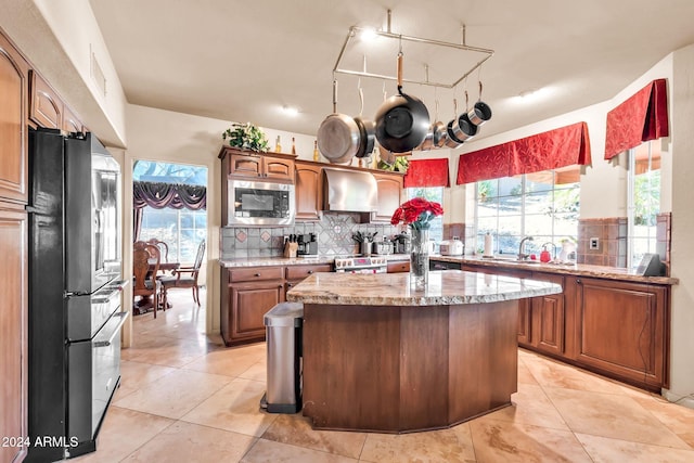 kitchen with sink, appliances with stainless steel finishes, backsplash, a kitchen island, and wall chimney exhaust hood