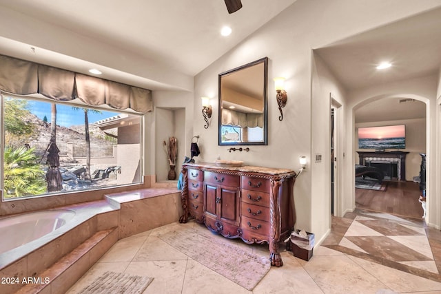 bathroom with tiled tub, vanity, and lofted ceiling