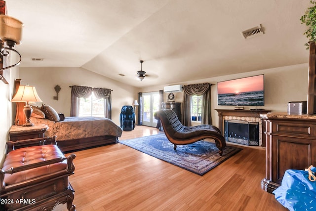 bedroom with an AC wall unit, lofted ceiling, ceiling fan, a premium fireplace, and light hardwood / wood-style flooring