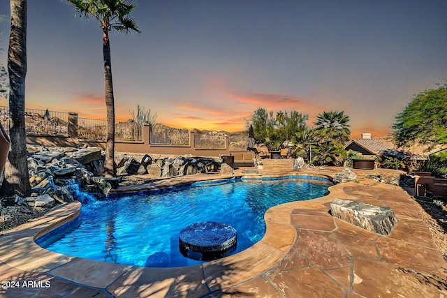 pool at dusk with pool water feature and a patio area