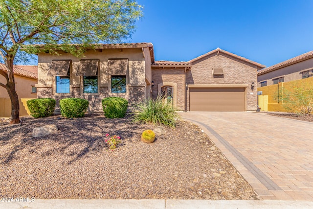 mediterranean / spanish-style home featuring a tiled roof, decorative driveway, a garage, and stucco siding