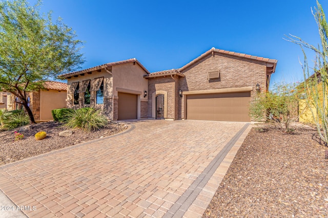 mediterranean / spanish home featuring a tiled roof, stucco siding, decorative driveway, a garage, and stone siding