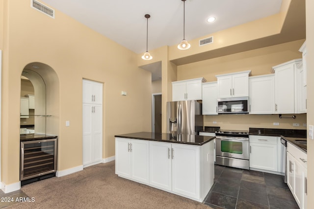 kitchen with dark colored carpet, white cabinetry, appliances with stainless steel finishes, beverage cooler, and a kitchen island