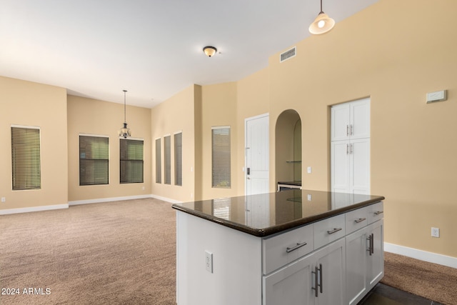 kitchen with dark stone counters, decorative light fixtures, dark carpet, a notable chandelier, and a center island