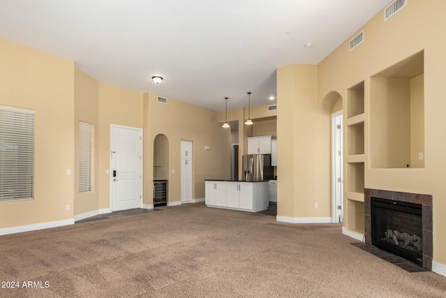 unfurnished living room with built in shelves, light colored carpet, and a tiled fireplace