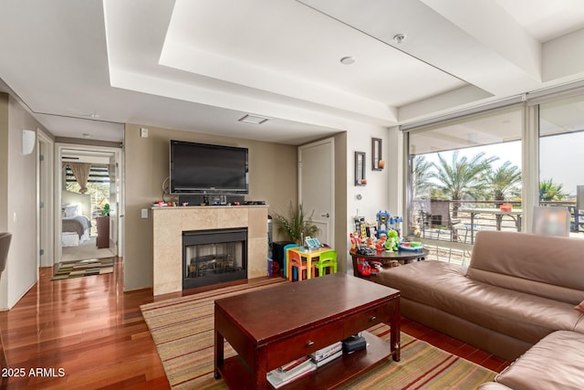 living area featuring wood finished floors, a raised ceiling, and a tiled fireplace
