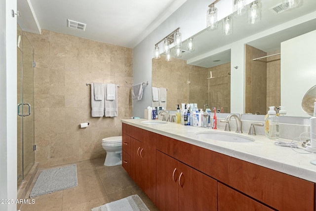 bathroom featuring tile walls, a shower stall, tile patterned flooring, toilet, and double vanity