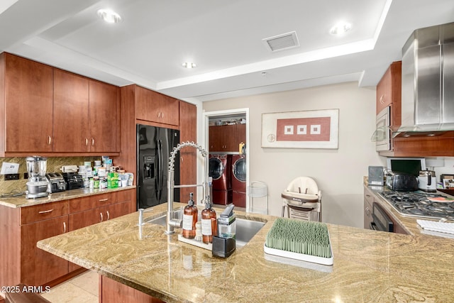 kitchen featuring black fridge, washer and dryer, light stone counters, brown cabinets, and recessed lighting