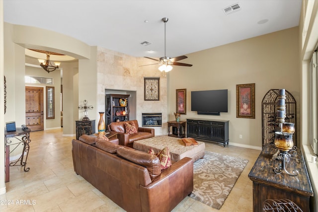 living room featuring a tiled fireplace and ceiling fan with notable chandelier