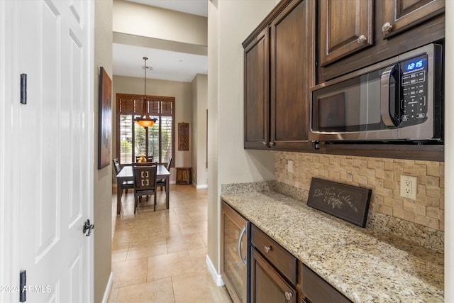 kitchen featuring light stone countertops, pendant lighting, tasteful backsplash, and dark brown cabinets