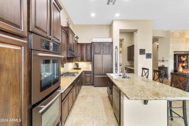 kitchen with light stone countertops, stainless steel appliances, a kitchen breakfast bar, an island with sink, and decorative backsplash