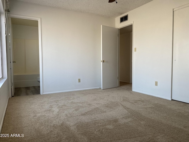 unfurnished bedroom featuring ensuite bath, light carpet, and a textured ceiling