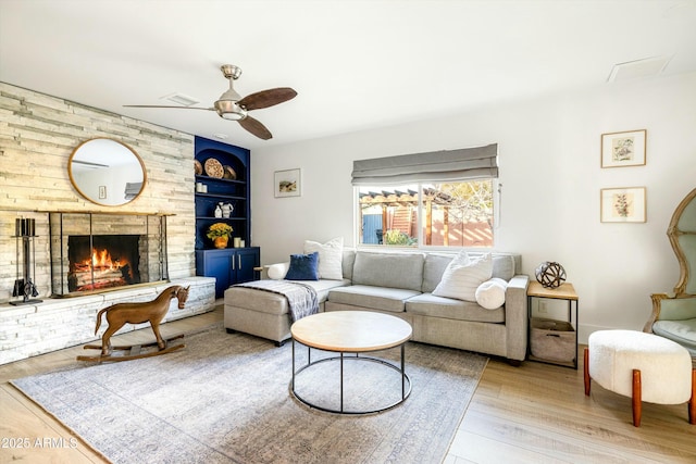 living area with built in shelves, a brick fireplace, wood finished floors, and a ceiling fan