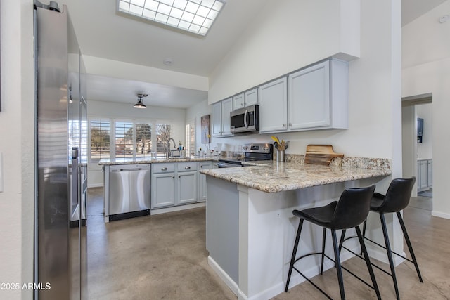 kitchen featuring appliances with stainless steel finishes, a sink, a kitchen breakfast bar, a peninsula, and baseboards