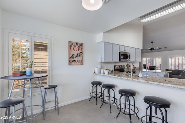 kitchen with a peninsula, baseboards, light stone counters, and stainless steel appliances