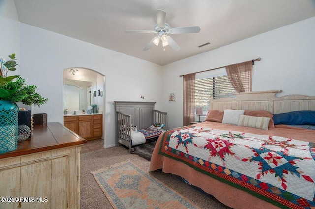 bedroom with light carpet, visible vents, arched walkways, a ceiling fan, and ensuite bathroom