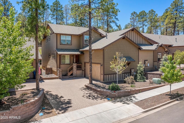 view of front facade featuring decorative driveway, a shingled roof, board and batten siding, a garage, and cooling unit