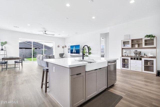 kitchen with dishwasher, sink, gray cabinetry, a kitchen island with sink, and light hardwood / wood-style floors