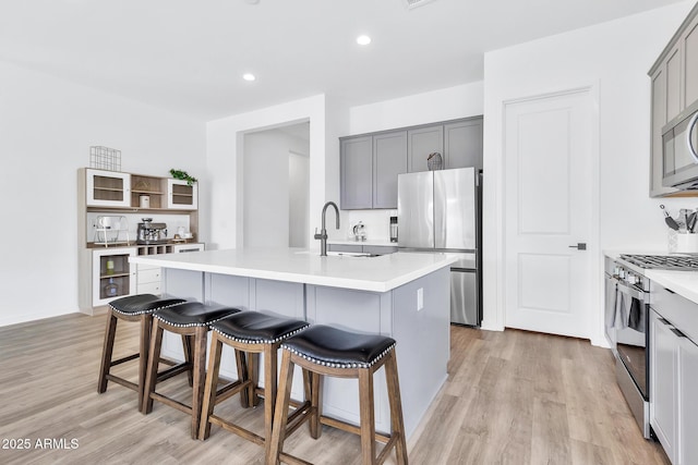 kitchen with sink, a breakfast bar area, appliances with stainless steel finishes, a center island with sink, and light wood-type flooring