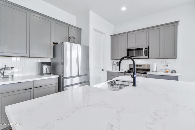 kitchen featuring tasteful backsplash, light stone countertops, gray cabinets, and stainless steel appliances