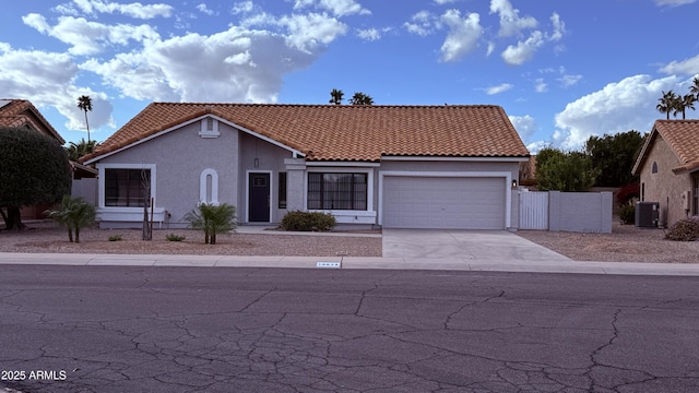 mediterranean / spanish house with a tile roof, stucco siding, concrete driveway, an attached garage, and central AC unit