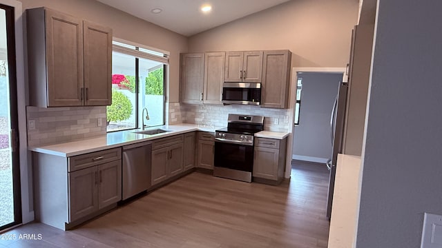 kitchen featuring stainless steel appliances, light countertops, vaulted ceiling, a sink, and wood finished floors