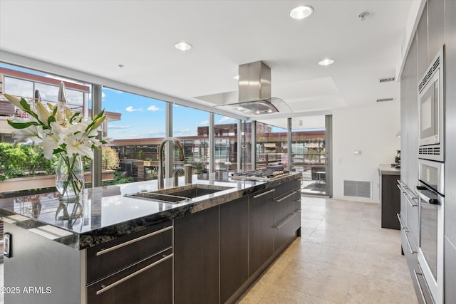 kitchen featuring a sink, a kitchen island with sink, island range hood, visible vents, and modern cabinets