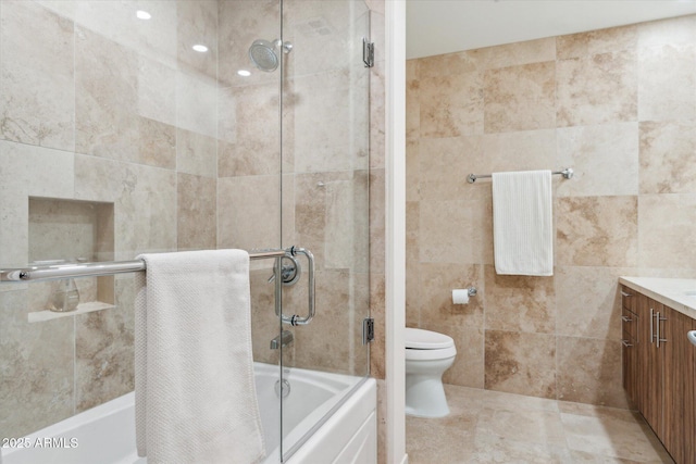 bathroom with shower / bath combination with glass door, toilet, tile walls, and vanity
