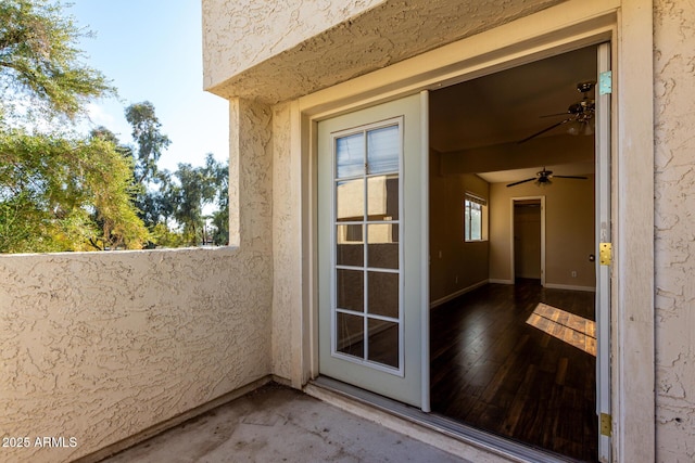 property entrance featuring a ceiling fan, a balcony, and stucco siding