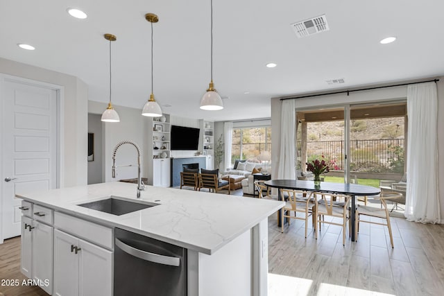 kitchen with sink, white cabinetry, light stone counters, hanging light fixtures, and dishwasher