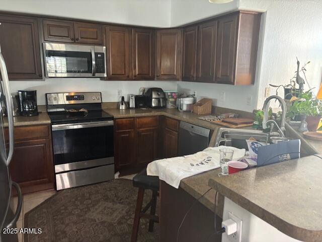 kitchen featuring sink, a kitchen breakfast bar, dark brown cabinetry, and stainless steel appliances