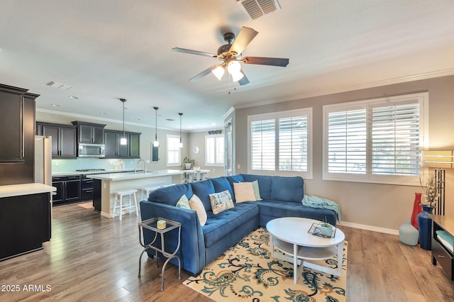 living room with baseboards, crown molding, a ceiling fan, visible vents, and wood finished floors