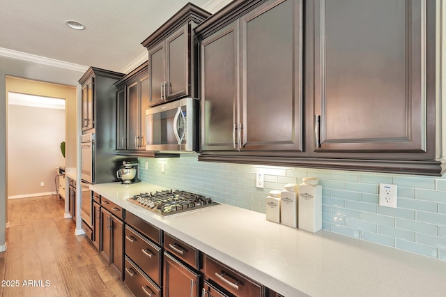 kitchen with ornamental molding, appliances with stainless steel finishes, light countertops, light wood finished floors, and backsplash