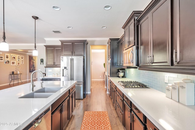 kitchen featuring hanging light fixtures, a sink, ornamental molding, light countertops, and appliances with stainless steel finishes