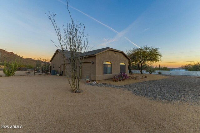 view of front of property featuring stucco siding, an attached garage, dirt driveway, and central AC unit