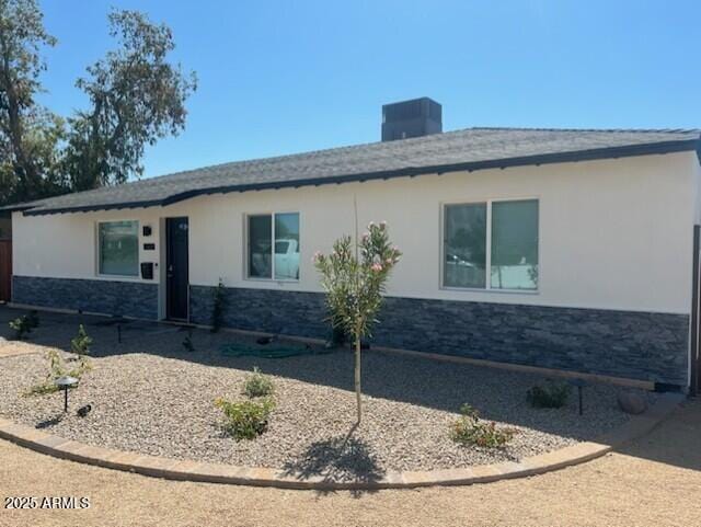 exterior space featuring central AC unit, a chimney, stucco siding, and stone siding