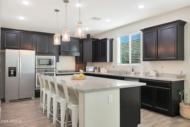 kitchen with light hardwood / wood-style flooring, sink, a kitchen island, pendant lighting, and appliances with stainless steel finishes