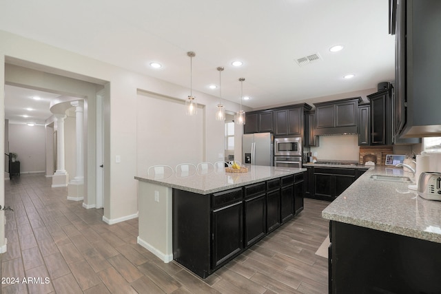 kitchen with appliances with stainless steel finishes, light stone countertops, a center island, ornate columns, and pendant lighting