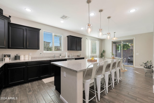 kitchen with light stone counters, a center island, hardwood / wood-style floors, a breakfast bar, and pendant lighting