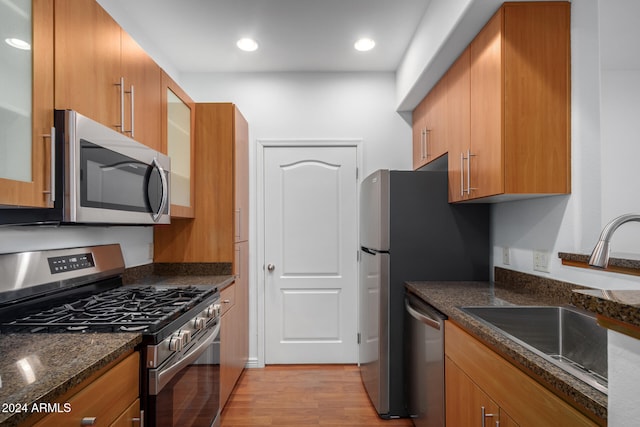 kitchen featuring dark stone counters, sink, appliances with stainless steel finishes, and light hardwood / wood-style flooring