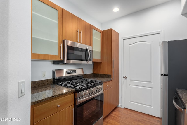 kitchen with appliances with stainless steel finishes, light hardwood / wood-style floors, and dark stone counters