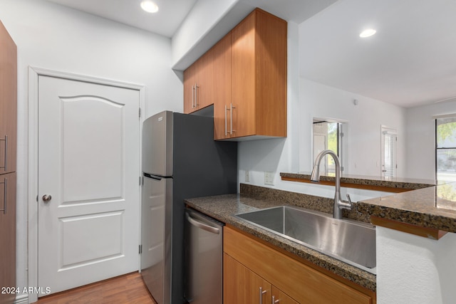 kitchen featuring dishwasher, sink, dark stone countertops, light hardwood / wood-style floors, and kitchen peninsula