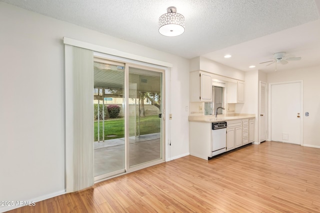 kitchen featuring white dishwasher, a textured ceiling, white cabinetry, light wood-type flooring, and sink